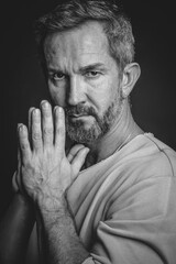 Fototapeta na wymiar Grey haired mature man put hands together looking at camera. Handsome middle aged man in black and white photo. Black and white portrait of attractive, beautiful, serious man