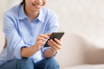 Unrecognizable lady sitting on sofa, using cell phone, cropped