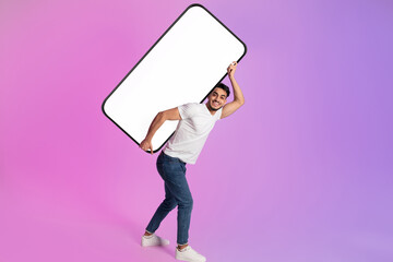 Full length portrait of cheery young Arab man carrying huge heavy mobile phone with empty screen in...