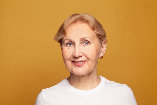 Cute Friendly Senior Woman Face On Bright Yellow Studio Background, Mature Model 60 Year Old