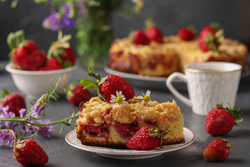 Homemade pie with strawberries and streusel with cut piece and also cup of coffee on dark gray table