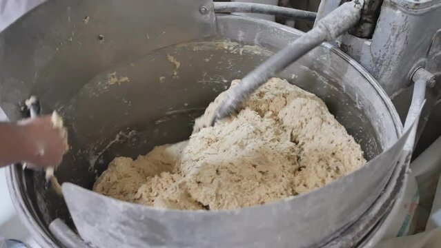 large industrial machine for kneading dough in the process. The baker's hand removes the dough with a spatula from the blade and walls of the dough mixer. Top view, slow motion