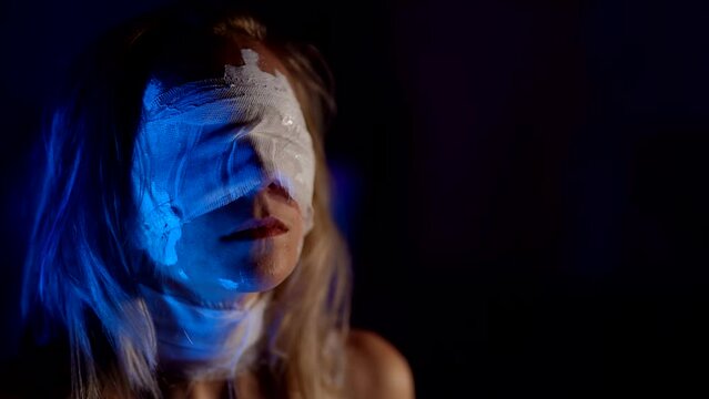 portrait of blindfolded woman in darkness, lady with bandages on eyes is standing alone in dark room