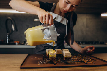 Woman pouring cream on a plate of layered brown cake with raspberry on top