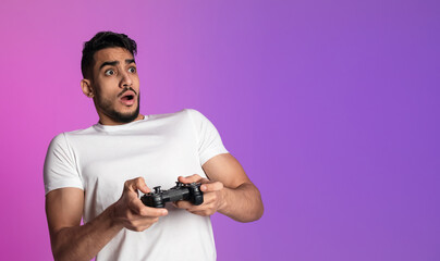 Shocked millennial Arab man with joystick playing video game in neon light, banner design with copy space