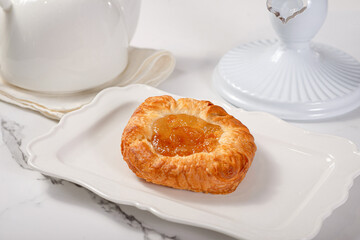 Fresh pastries on a white plate on a marble white table among white dishes with coffee and tea