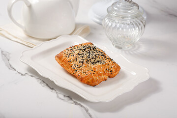 Fresh pastries on a white plate on a marble white table among white dishes with coffee and tea