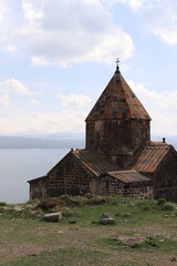 Fototapeta na wymiar The temple of the ancient Sevanavank monastery on Lake Sevan in Armenia and fragments of the destroyed monastery wall. Holy historical sites in Amenia.