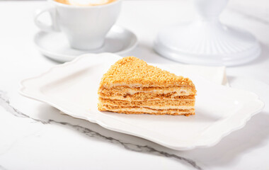 A piece of Napoleon cake on a light marble table among white dishes