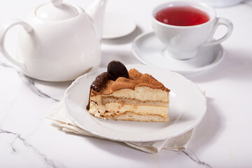 A piece of Tiramisu cake on a white saucer on a white marble table in a cafe