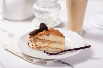 A piece of Tiramisu cake on a white saucer on a white marble table in a cafe