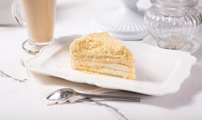 A piece of Napoleon cake on a light marble table among white dishes