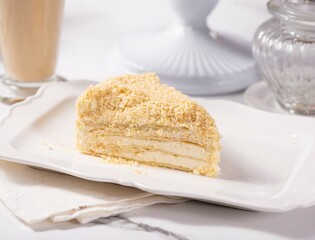 A piece of Napoleon cake on a light marble table among white dishes