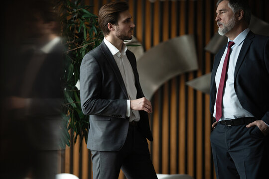 Two businessmen deep in discussion together while standing in modern office.
