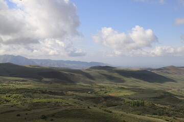 Green mountain valleys of Armenia under blue sky and clouds on a sunny day. Shadows from the clouds fall on the slopes and the valley and form bizarre shadows.