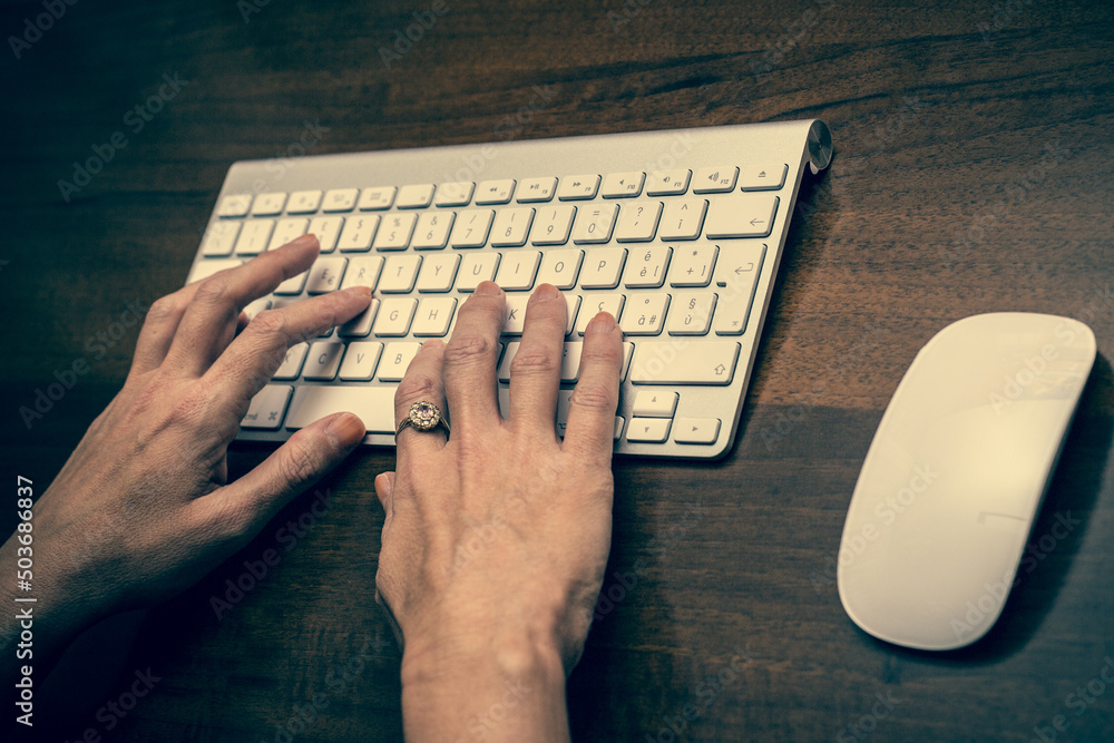 Poster closeup shot of hands typing on the keyboard and the mouse on a table
