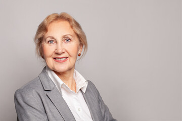 Blonde senior business woman standing over gray background. Happy lady smiling and looking at the camera. Positive person.