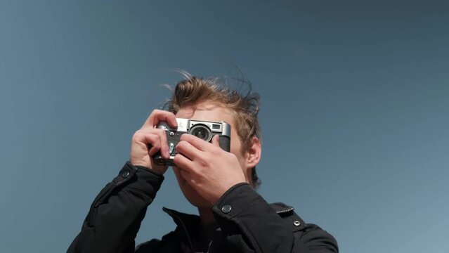 A blond man takes a close-up photo with a retro camera on a sunny day. . High quality 4k footage