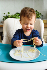 Little cute baby learning to eat himself at the kids table in the kitchen. It feels happy.