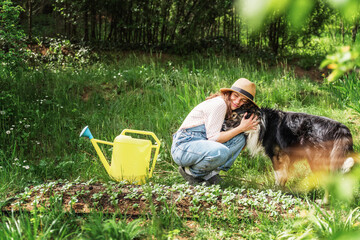 Beautiful young woman in a hat hugging her dog and taking care of her garden