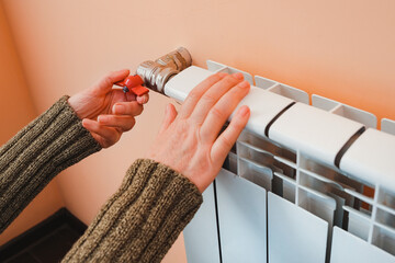 A woman's hand holds the heating thermostat handle. Heating service cost concept, utility price...