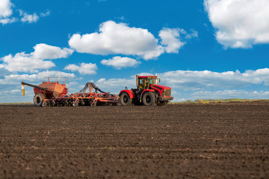 tractor harrowing by plows and seeding large soil field blue cloudy sky day background in spring season