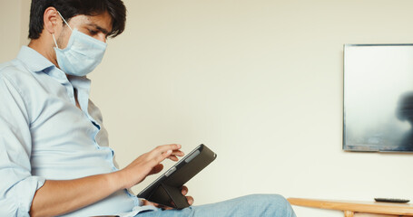 Young man tapping on his tablet while wearing a face mask in his office