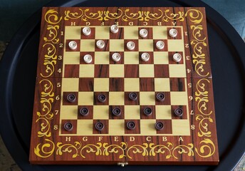 Board game of checkers - a wooden board with placed checkers stands on a round black metal table in the living room.