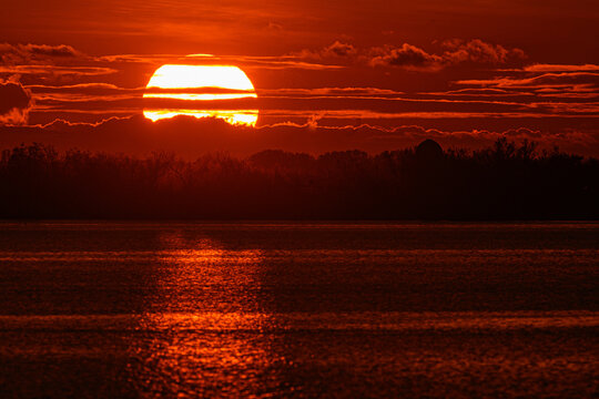 Sole rosso al tramonto con riflesso e luccichio sul mare e nuvole in lontananza