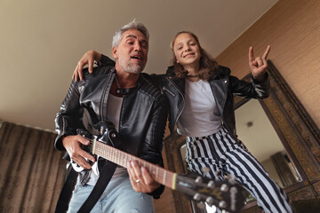 Father rock guitarist having fun and and dancing with his teenage daughter at home.