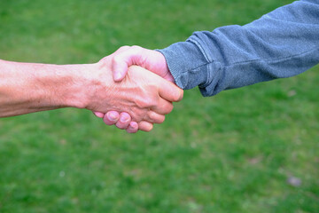 close-up of male hands hold a handshake against the background of green grass, the concept of a meeting of friends, the joy of communication in an informal setting, a European greeting