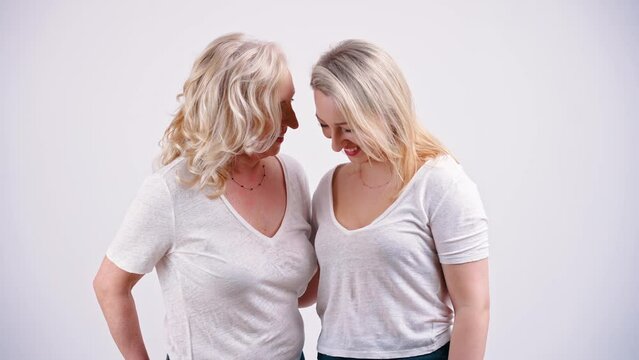Mother and daughter like sisters wearing similar clothes standing close to each other and laughing. Studio shot on white background. High quality 4k footage