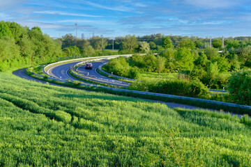 high-speed asphalt road in europe, green trees and bushes on sides, sharp turn, multi-lane car interchange, trucks driving, concept of traveling, way to work, traffic safety, cargo transportation