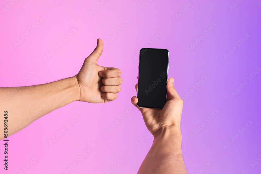 Poster Unrecognizable millennial man showing smartphone with empty screen, gesturing thumb up in neon light, mockup