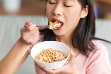 Healthy diet concept. Korean lady eating cereals with yoghurt, having nutritious breakfast at home, closeup
