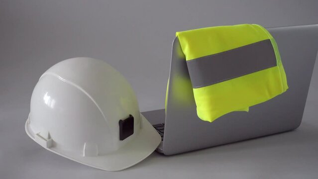 Construction, design, architecture or building industry concept. White safety helmet, reflective vest and laptop computer on engineer's table. High quality 4k video footage