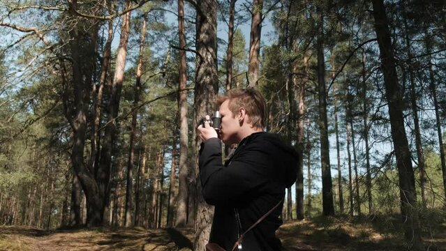 A blond man takes pictures with a retro camera. A man takes a photo of a forest landscape. High quality 4k footage