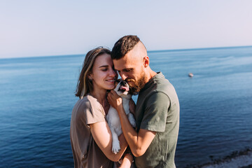 Happy couple with favourite pet. Young man and woman have walk near sea.