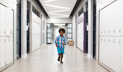 Full length of smiling african american elementary schoolboy running in corridor with lockers