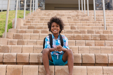 Portrait of smiling african american elementary schoolboy sitting on school building steps