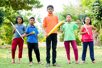 Group of teenager kids with bat, ball and stumps ready for playing cricket by looking camera at park - concept of confident, childhood lifestyle and leisure activities