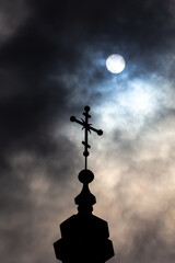 Fototapeta na wymiar Orthodox cross on top of the church against the dramatic sky. Photo taken against the sun behind the clouds.