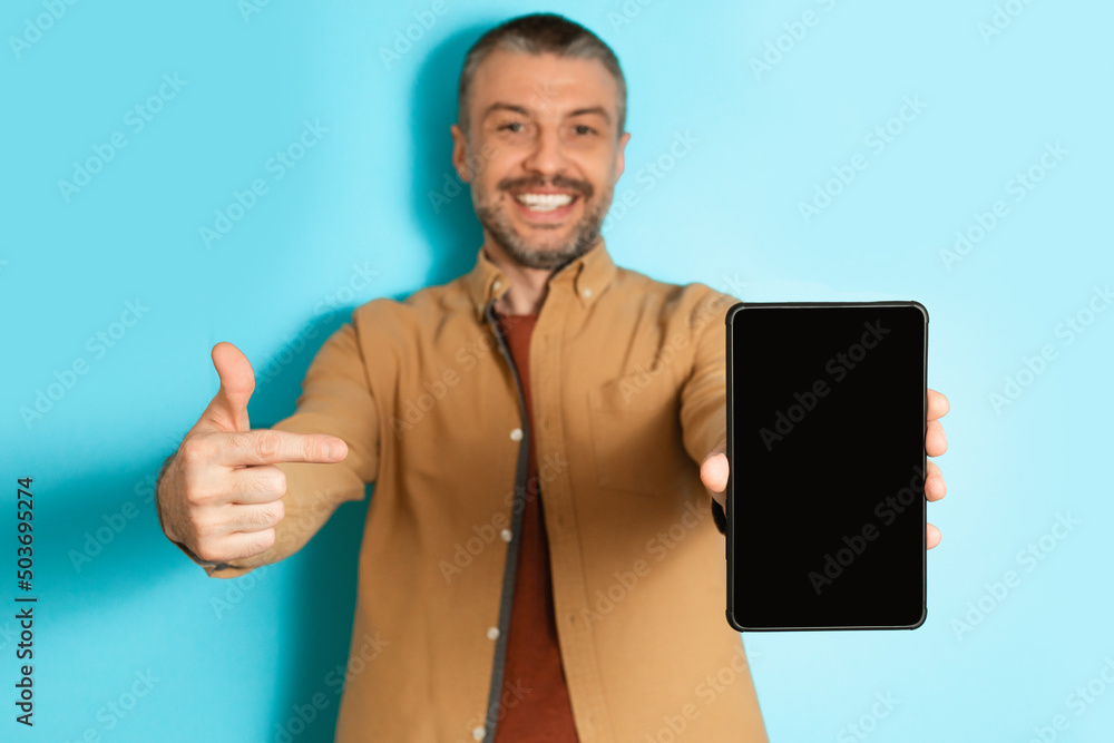 Poster man showing digital tablet pointing finger at screen, blue background