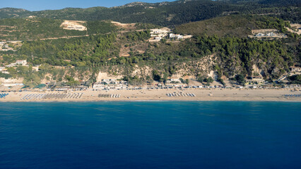 Aerial view of beautiful sandy beach with sunshades and soft turquoise ocean wave. Tropical sea in summer season on Kathisma beach on Lefkada island.