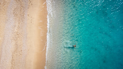 Aerial view of man swimming in the shallow sea water, enjoying beach and soft turquoise ocean wave. Tropical sea in summer season on Egremni beach on Lefkada island.