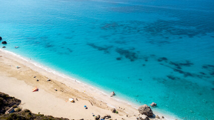 Aerial view of beautiful sandy beach with sunshades and soft turquoise ocean wave. Tropical sea in summer season on Megali Petra beach on Lefkada island.