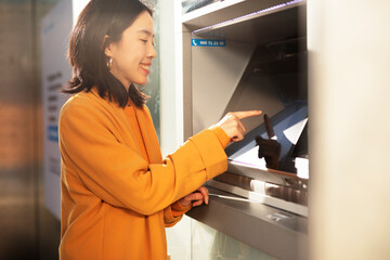 Happy smiling young woman withdrawing money from credit card. Young woman typing pin code on keypad of ATM machine...