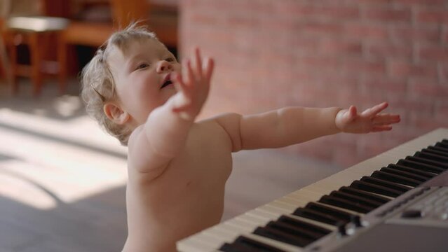 Asian baby girl toddler playing electric piano, sit down on the floor tapping on keyboard music instrument, kids artistry learning skills, happy healthy female child pretend to play music by herself