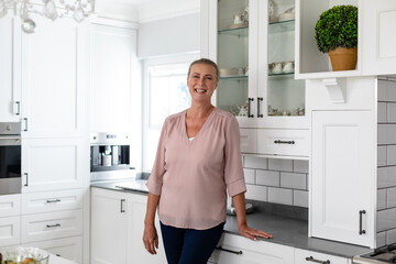 Fototapeta na wymiar Portrait of happy senior caucasian woman standing by kitchen counter at home