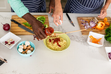 Obraz na płótnie Canvas Midsection of senior multiracial couple preparing noodles at kitchen island